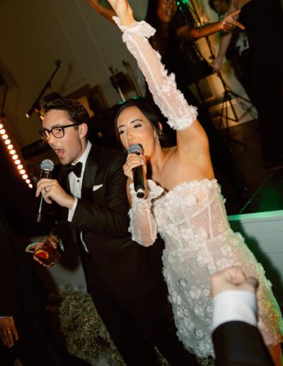 Groom wearing a custom tuxedo from Tailored Gents at Savile Row singing with his bride.
