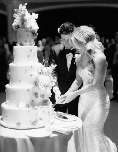 Groom wearing a custom wedding tuxedo from Tailored Gents at Savile Row cutting the cake with his bride.
